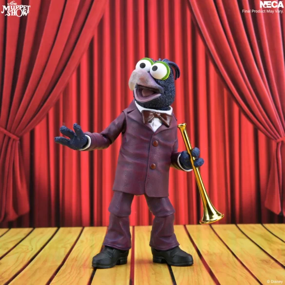Gonzo de NECA con una trompeta dorada y una mano extendida frente al telón rojo.