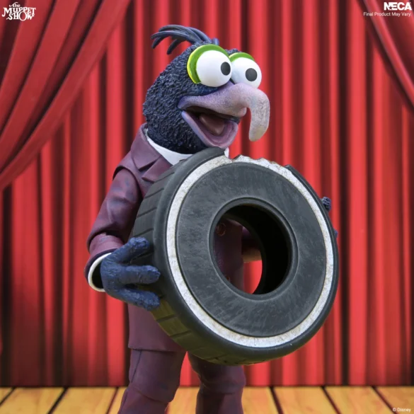 Gonzo de NECA sostiene un neumático negro frente al telón de The Muppet Show.