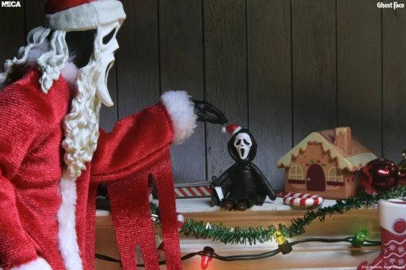 Santa’s Slay Ghost Face de NECA junto a una mesa con accesorios navideños.